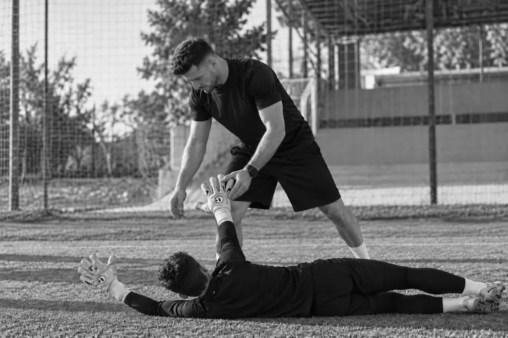 Entrenador junto a un arquero tendido en el césped